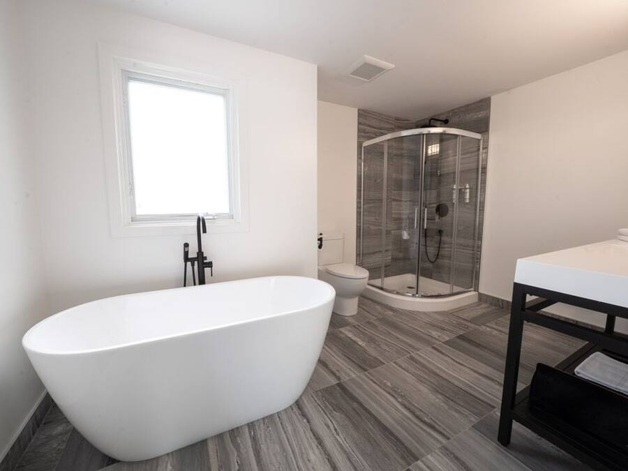 Un baño moderno con una bañera independiente, ducha con mampara de vidrio y tocador blanco.