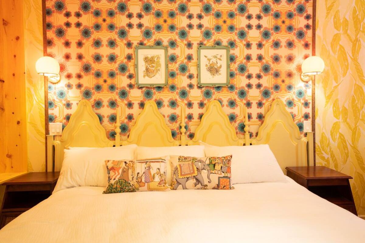 Ein Hotelzimmer mit einem Bett, zwei Nachttischen, einer Wand mit einem Muster und zwei gerahmten Bildern.