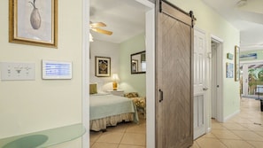 A hotel room with a bed, bedside table, lamp, and a sliding door leading to another room.