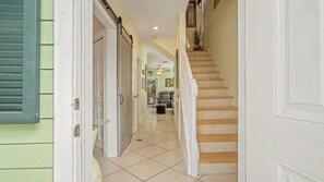 A hallway with a staircase leading to a second floor, a door with a glass shelf, and a ceiling fan.