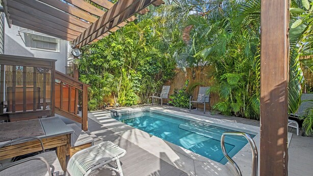 Un espace piscine doté d’une terrasse en bois, de chaises longues et d’une pergola.