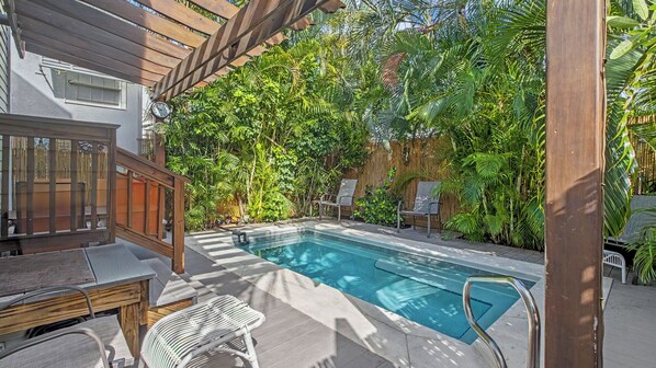 A pool area with a wooden deck, lounge chairs, and a pergola.
