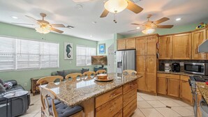 Une cuisine moderne avec des meubles en bois, des plans de travail en granit, un îlot central, des ventilateurs de plafond et un grand réfrigérateur.