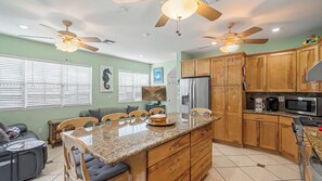 A modern kitchen with wooden cabinets, granite countertops, a central island, ceiling fans, and a large refrigerator.