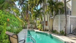 A pool area with a clear water surface, surrounded by palm trees and a white lattice fence. - Campbell Suite (Key West)