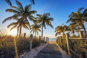 A wooden boardwalk leading to a beach with palm trees and a clear sky. - Campbell Suite (Key West)