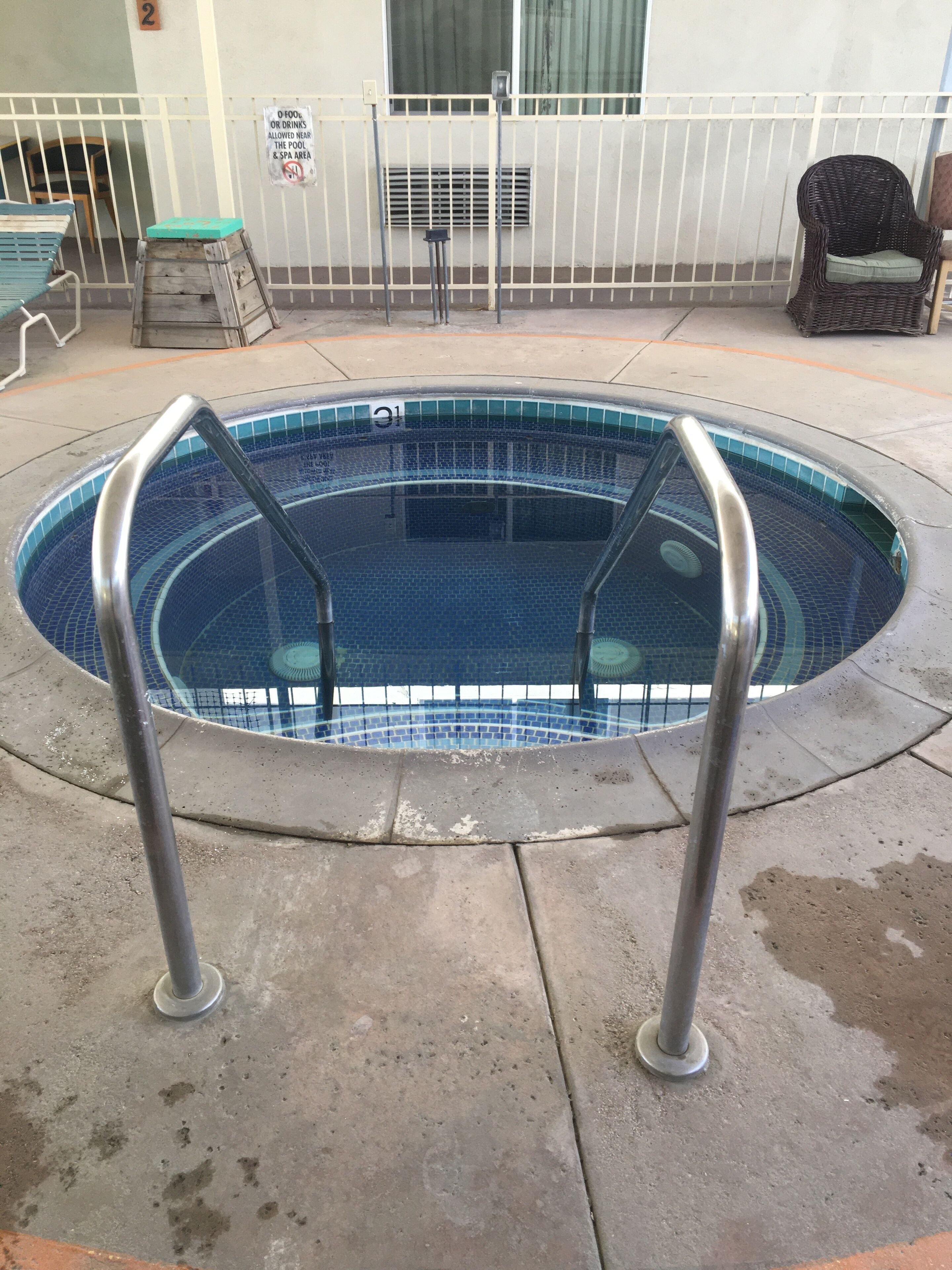 A swimming pool with metal handrails, a tiled edge, and a concrete deck.