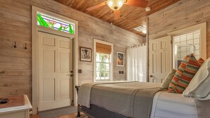 A bedroom with a bed, a door with a stained glass window, and a ceiling fan. - Conch Republic Retreat (Key West)