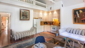 A spacious living area with a high ceiling, a dining table, a sofa, and a kitchen with white cabinets and a tiled backsplash. - Conch Republic Retreat (Key West)