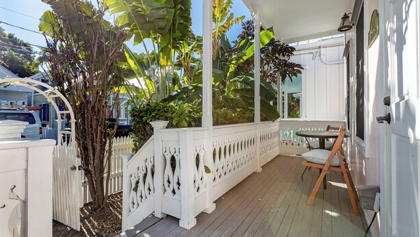 A covered porch with a white railing, a table with a chair, and a small tree. - Conch Republic Retreat (Key West)