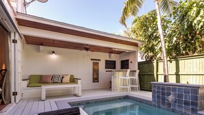 A poolside area with a wooden ceiling, a white bench, a green cushion, and a tiled pool edge. - Conch Republic Retreat (Key West)