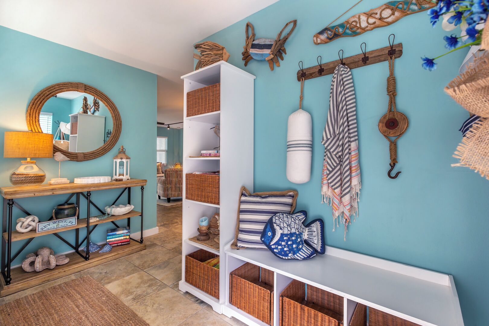 Une pièce avec un mur de couleur turquoise, une console blanche, des paniers en osier et un miroir encadré d’une corde.