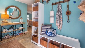 A room with a teal wall, a white console table, wicker baskets, and a mirror with a rope frame. - Duval Square (Key West)