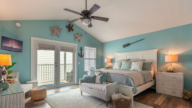 A bedroom with a bed, nightstands, a ceiling fan, a large window, and a view of the outdoors. - Duval Square (Key West)