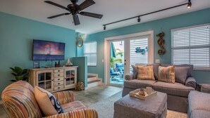 A living room with a teal wall, a ceiling fan, a TV, a cabinet, and a sofa with striped cushions. - Duval Square (Key West)