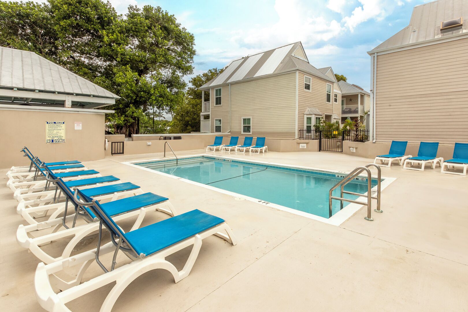 A pool area with lounge chairs, a pool, and a building with a sloped roof.