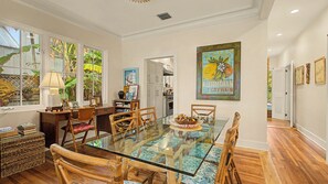A dining area with a glass table, wooden chairs, and a kitchen in the background.