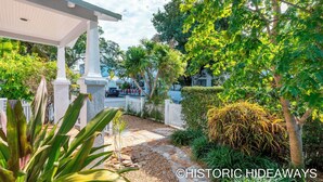A covered patio area with a stone pathway leading to a white fence. - Poinciana House (Key West)