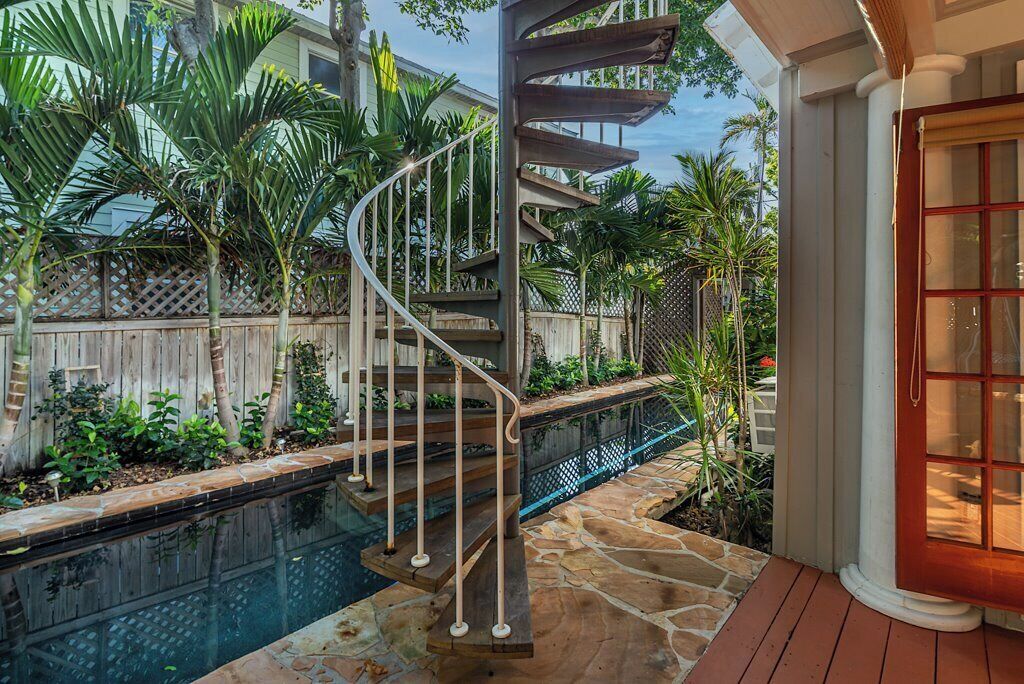 A spiral staircase leading to a pool area with a wooden deck and tropical plants.