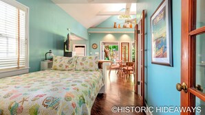A bedroom with a bed, a desk, and a chair. There is a window with blinds, a door, and a picture on the wall. - Poinciana House (Key West)