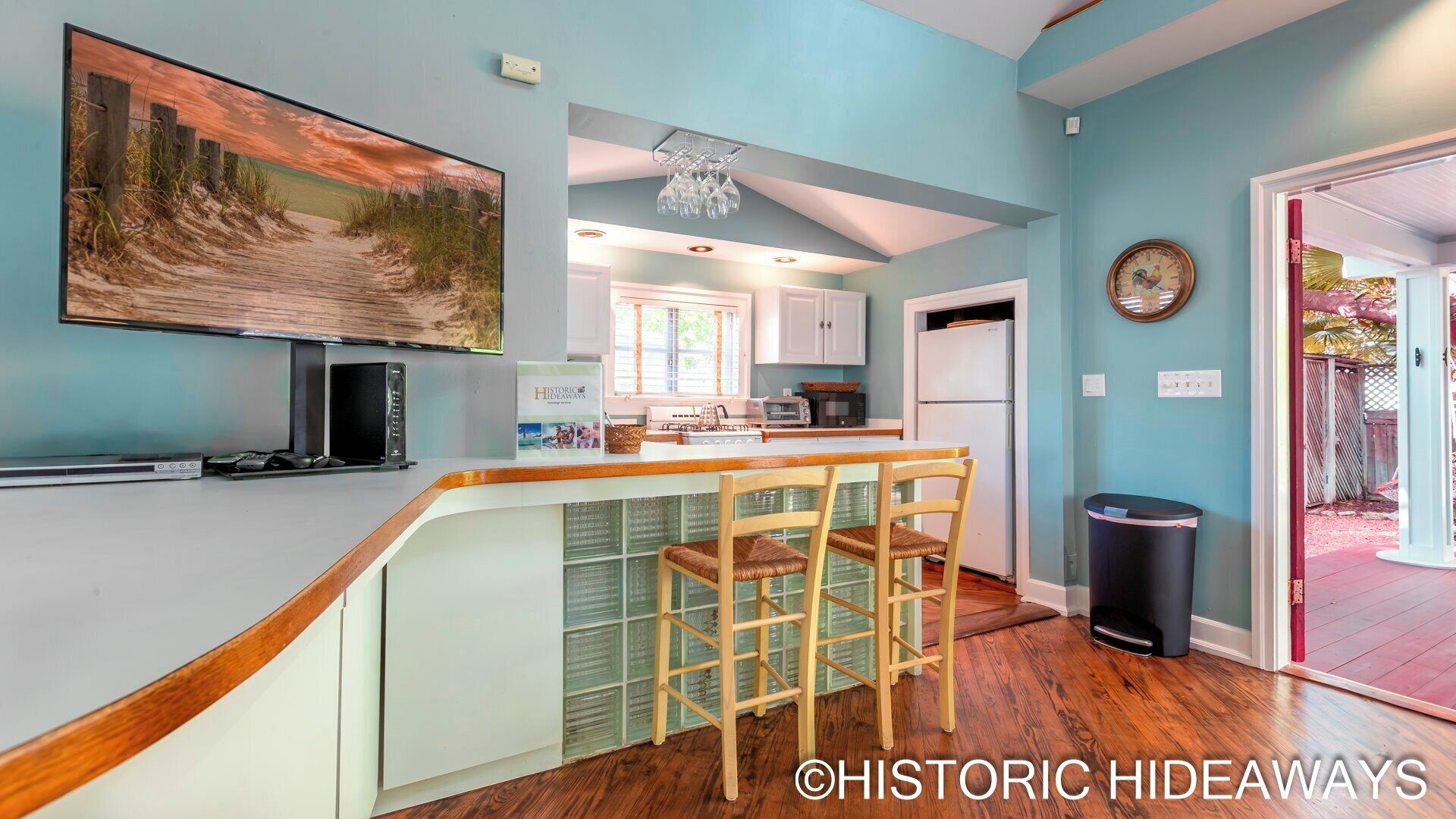 A kitchen with a bar area, wooden chairs, and a large painting on the wall.