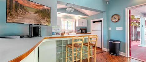 A kitchen with a bar area, wooden chairs, and a large painting on the wall.