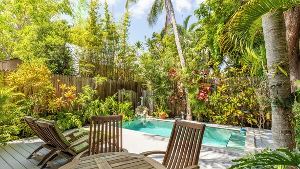 A wooden deck with a pool, surrounded by lush tropical plants and a wooden fence. - Quilted Giraffe (Key West)