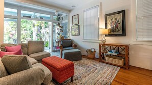 A cozy living room with a sofa set, a chair, a small ottoman, a patterned rug, and a wooden side table with a lamp. - Quilted Giraffe (Key West)