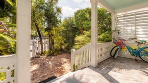 A covered porch with a bicycle parked by the railing. - Quilted Giraffe (Key West)
