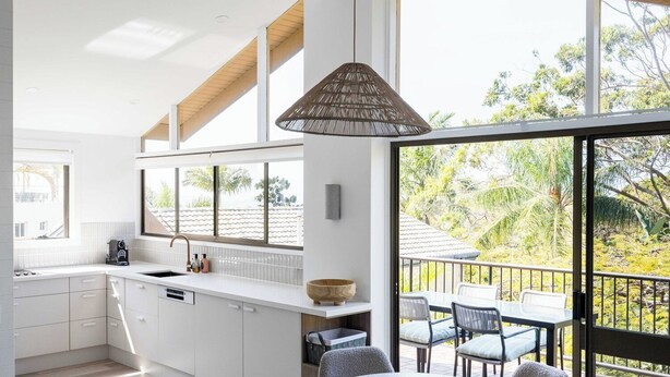 A modern kitchen with white cabinetry, a large window, and a dining area with outdoor seating.