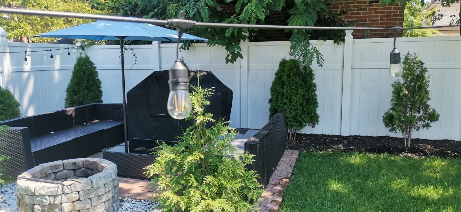 A backyard with a stone fire pit, a black grill, outdoor furniture, and a hanging light fixture.