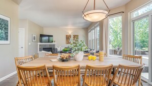 A dining area with a wooden table, chairs, a vase with flowers, and a television in the background. - Hot Tub + Deck | Walk to Pickleball | Near Central Bend | Canal Trail Base Camp (Bend)