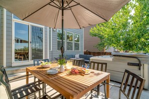 A wooden patio table with a beige umbrella, surrounded by chairs.