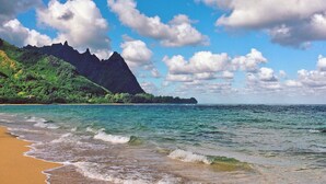 Une plage aux eaux turquoise et limpides, un rivage sablonneux et une montagne en arrière-plan.