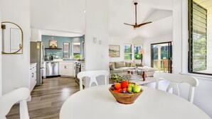 Une cuisine moderne avec des meubles blancs, un coin repas avec une table et des chaises blanches, et un salon avec un canapé et une table basse.