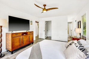 Ein Hotelzimmer mit einem großen Bett, einer Holzkabine mit einem Flachbildfernseher, einem Deckenventilator und einer Tür zu einem anderen Raum.