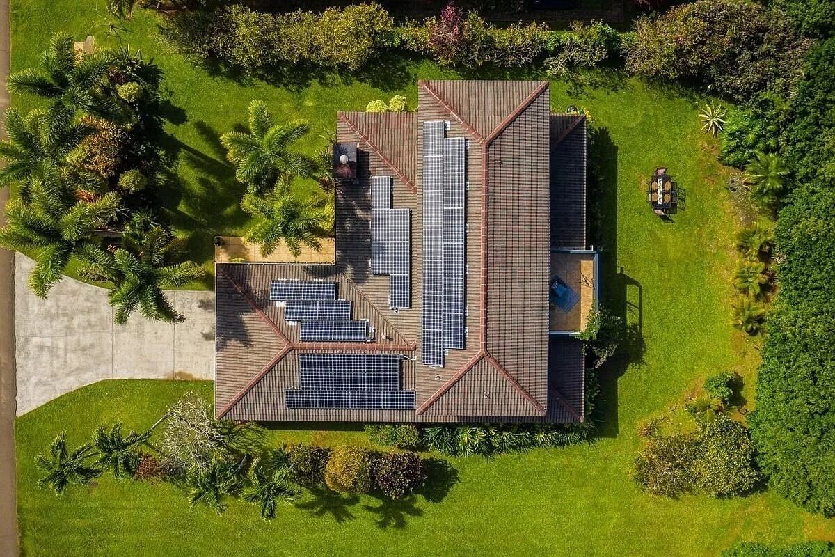 Een modern gebouw met een schuin dak, omringd door weelderige begroeiing en palmbomen.