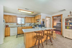 A kitchen with wooden cabinets, a central island with bar stools, a microwave, and a bookshelf.