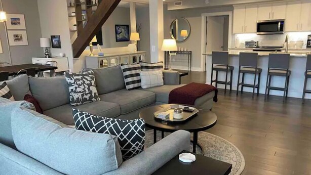 Un salon moderne avec un canapé gris, une table basse et un escalier menant à un espace cuisine.