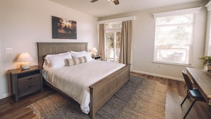 A bedroom with a wooden bed, two bedside tables with lamps, a ceiling fan, a large window with curtains, and a view of the outdoors. - Ranch House Interior - 4 bedroom, 4 bath home on-site of Galway Downs (Temecula)