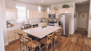 A modern kitchen with white cabinets, stainless steel appliances, and a central island with chairs. - Ranch House Interior - 4 bedroom, 4 bath home on-site of Galway Downs (Temecula)