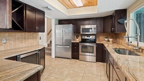 A modern kitchen with dark wood cabinets, stainless steel appliances, a granite countertop, and a skylight.