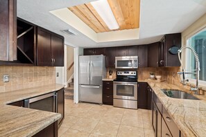A modern kitchen with dark wood cabinets, stainless steel appliances, a granite countertop, and a skylight.