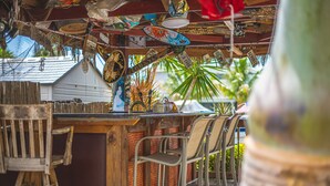 A bar area with metal chairs, a wooden bar counter, and various decorative items hanging from the ceiling.