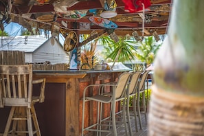A bar area with metal chairs, a wooden bar counter, and various decorative items hanging from the ceiling.