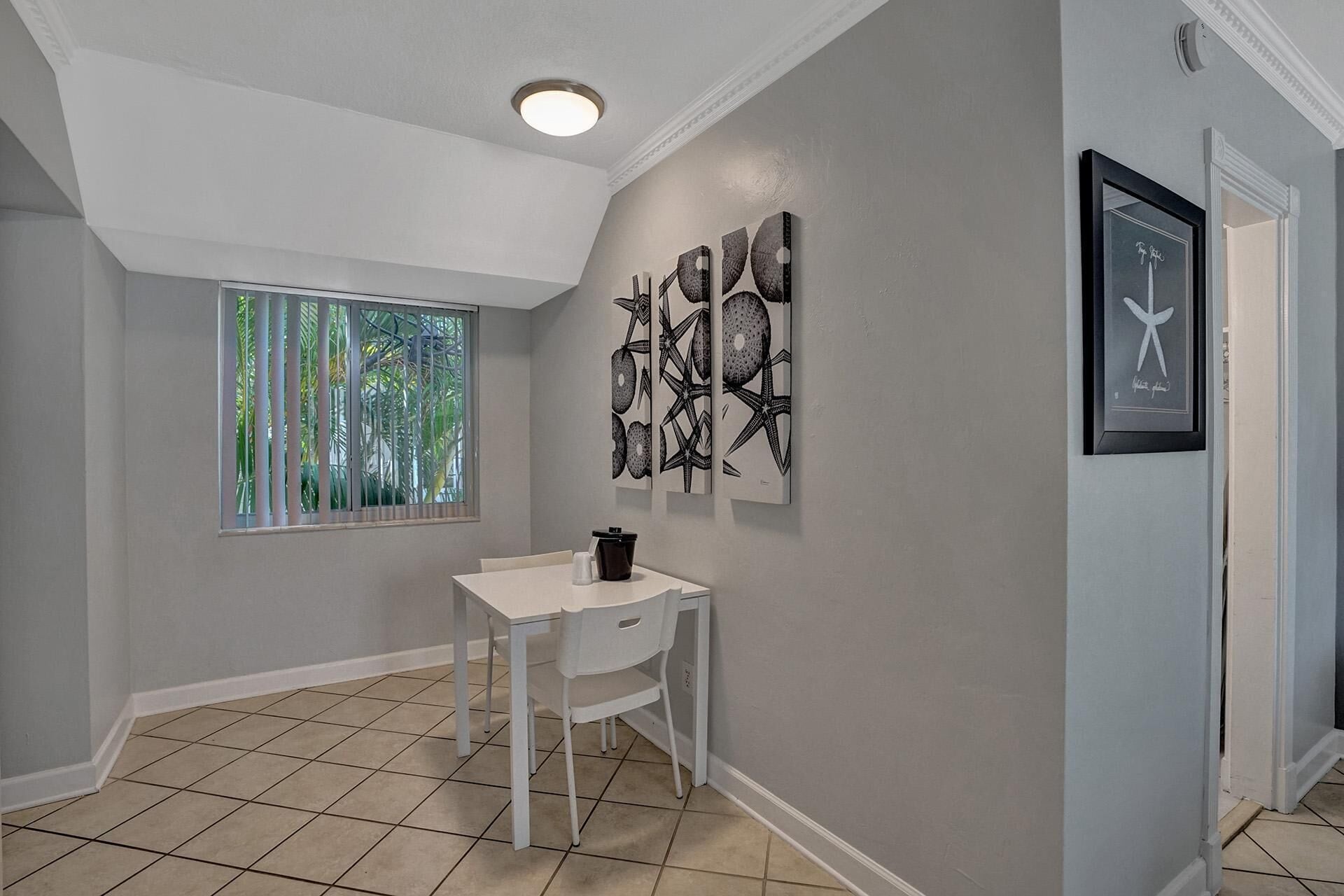 A hallway with a white desk, a window with vertical blinds, and three framed artworks on the wall.