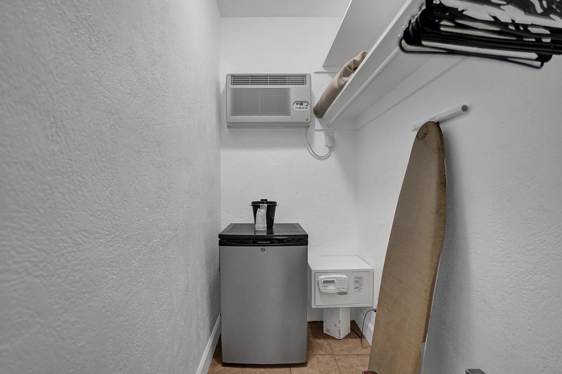 A compact bathroom with a white wall, a small sink, a white toilet, a compact heater, and a towel hanging on the wall.