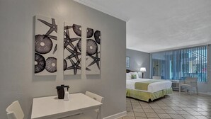 A hotel room with a bed, a desk, chairs, and artwork on the wall. - The Grand Resort and Spa  (Fort Lauderdale)