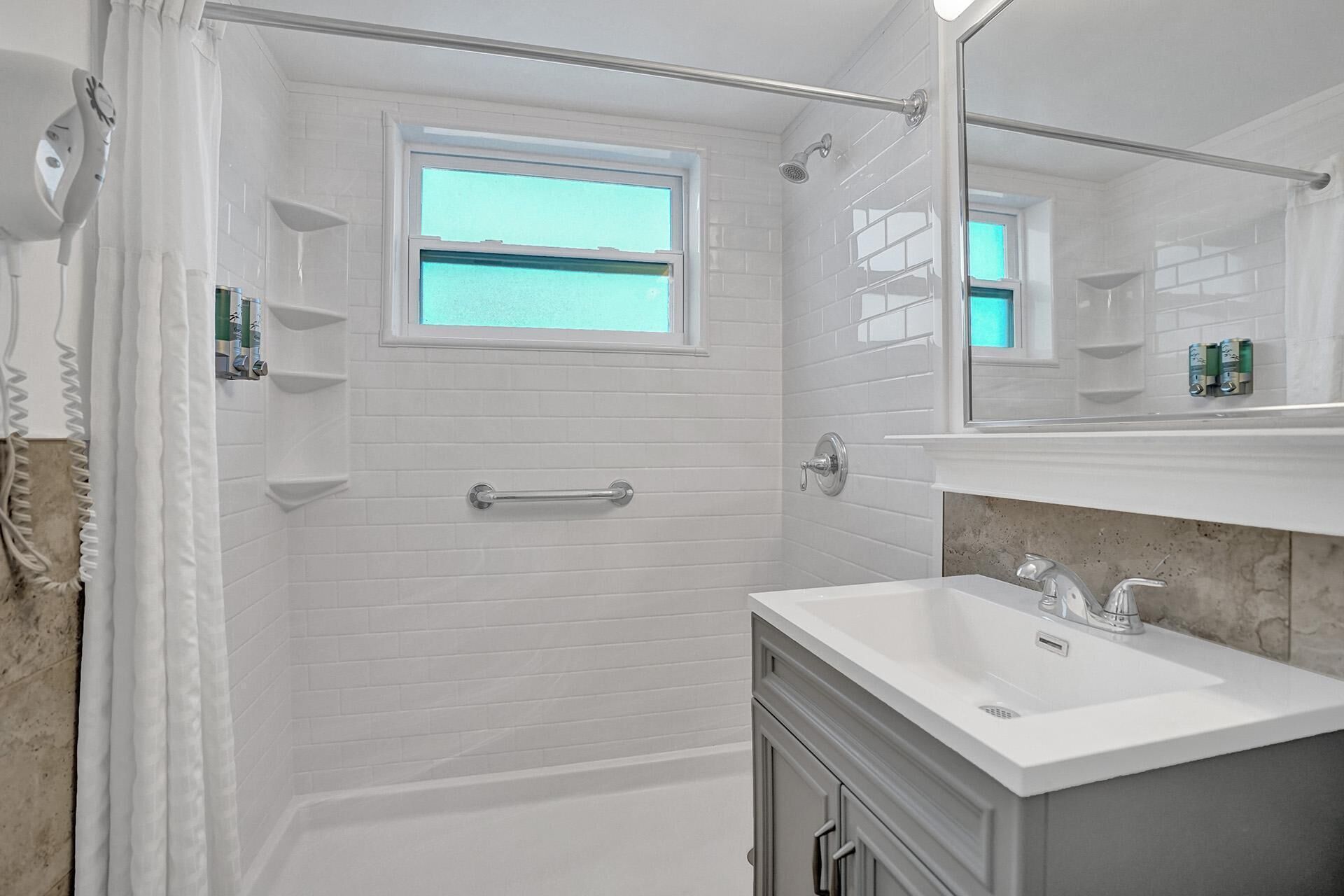 Une salle de bain moderne avec des carreaux de métro blancs, une douche avec une porte en verre, une fenêtre et un meuble-lavabo avec un évier et un miroir.