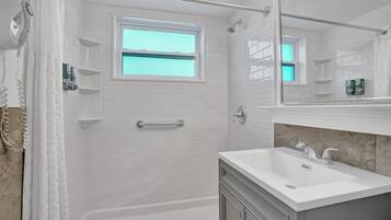 Une salle de bain moderne avec des carreaux de métro blancs, une douche avec une porte en verre, une fenêtre et un meuble-lavabo avec un évier et un miroir.